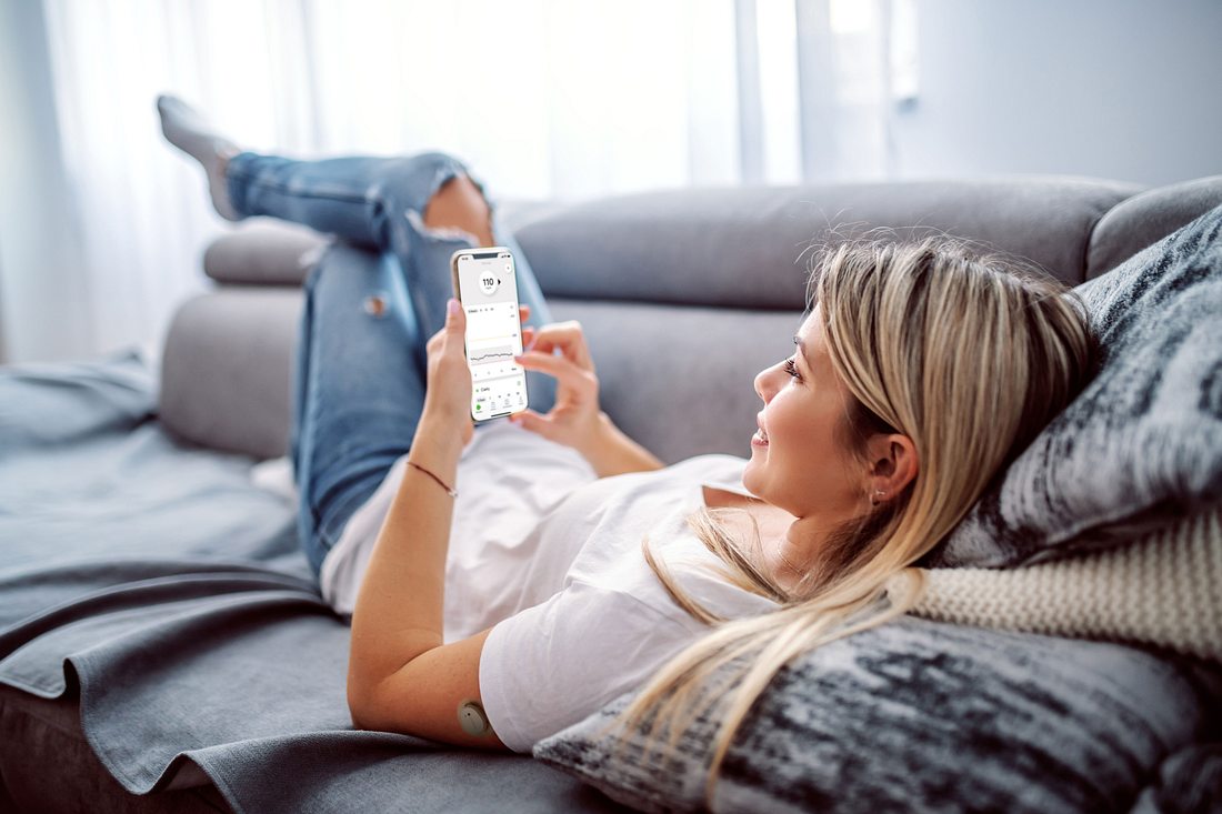 Dexcom G7 Frau auf dem Sofa schaut auf ihr Handy