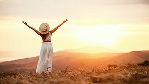 Glückliche Frau, die im Sommer mit dem Rücken zum Sonnenuntergang in der Natur steht - Foto: iStock / evgenyatamanenko