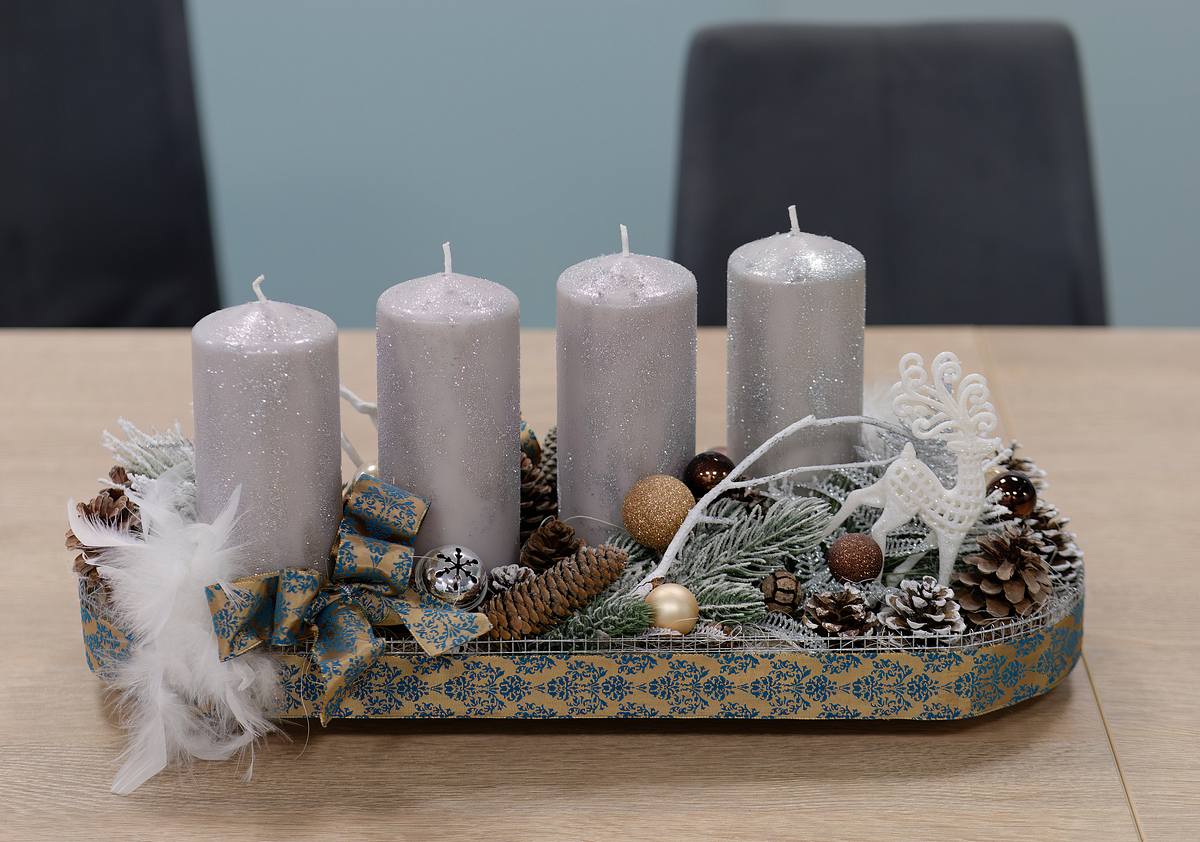 Ein Adventsgesteck mit silbernen Kerzen und Dekoration die an einen Winterwald erinnert