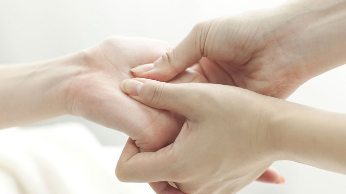 Frau drückt bei einer anderen Frau Akupressurpunkte an der Hand. 