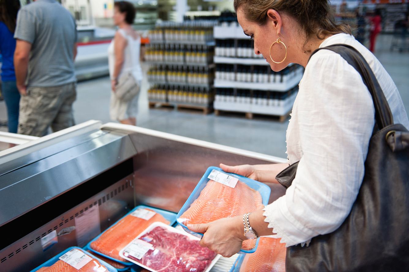 Eine Frau sucht im Supermarkt nach passendem Fleisch.