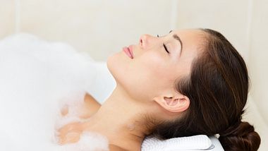 Frau in gefüllter Badewanne mit Badewannenkissen - Foto: iStock/ariwasabi