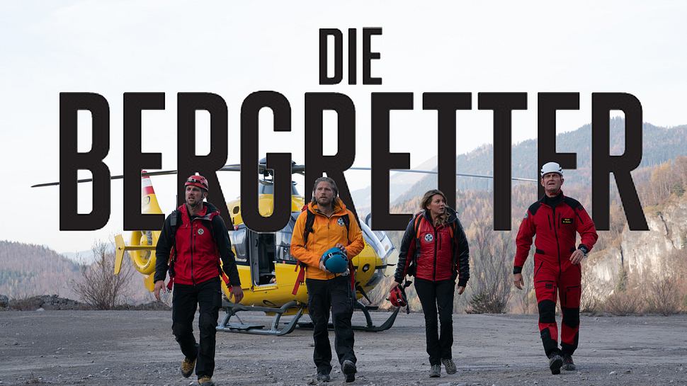 Die Bergretter-Hauptdarsteller laufen über einen Schotterplatz, hinter ihnen schwebt das Logo - Foto: ZDF / Martin Zwanzger / Stephanie Kulbach (Bearbeitung und Montage: Liebenswert)