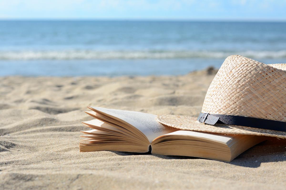 Strohhut am Strand neben einem Buch