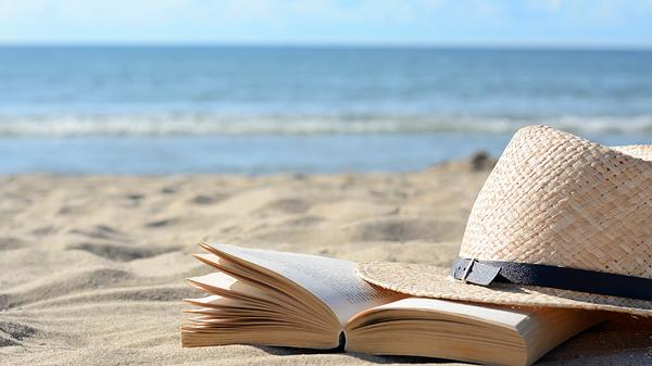 Strohhut am Strand neben einem Buch - Foto: Liudmila Chernetska / iStock