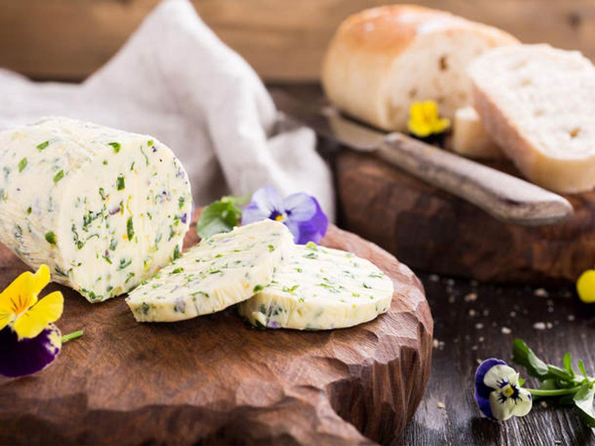 Gartenkräuterbutter mit Blüten auf einem Holzbrett.