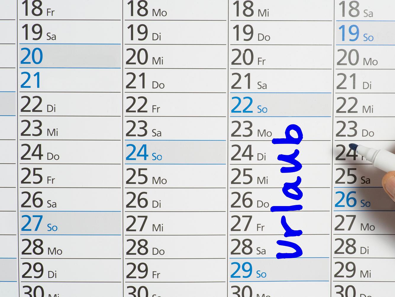 Frau trägt ihre Urlaubstage in einem Wandkalender ein. Frau trägt ihre Urlaubstage in einem Wandkalender ein.