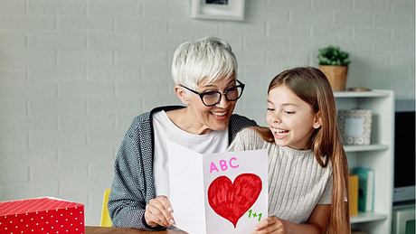 Oma liest ihrer Enkelin die Einschulungskarte vor - Foto: iStock/Paperkites