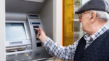 Älterer Mann hebt Geld am Automaten ab. 