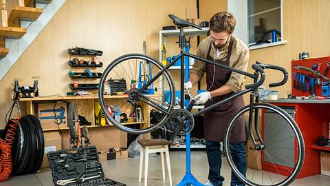 Mann repariert Fahhrad auf einem Fahrrad-Montageständer. - Foto: iStock/ shironosov