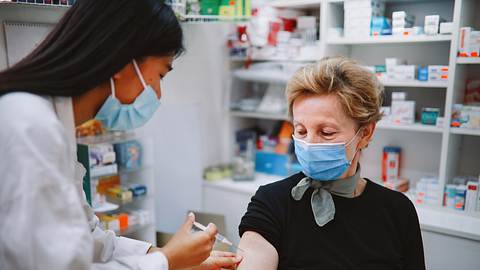 Eine Frau mit Mundschutz wird geimpft.  - Foto: iStock / lechatnoir