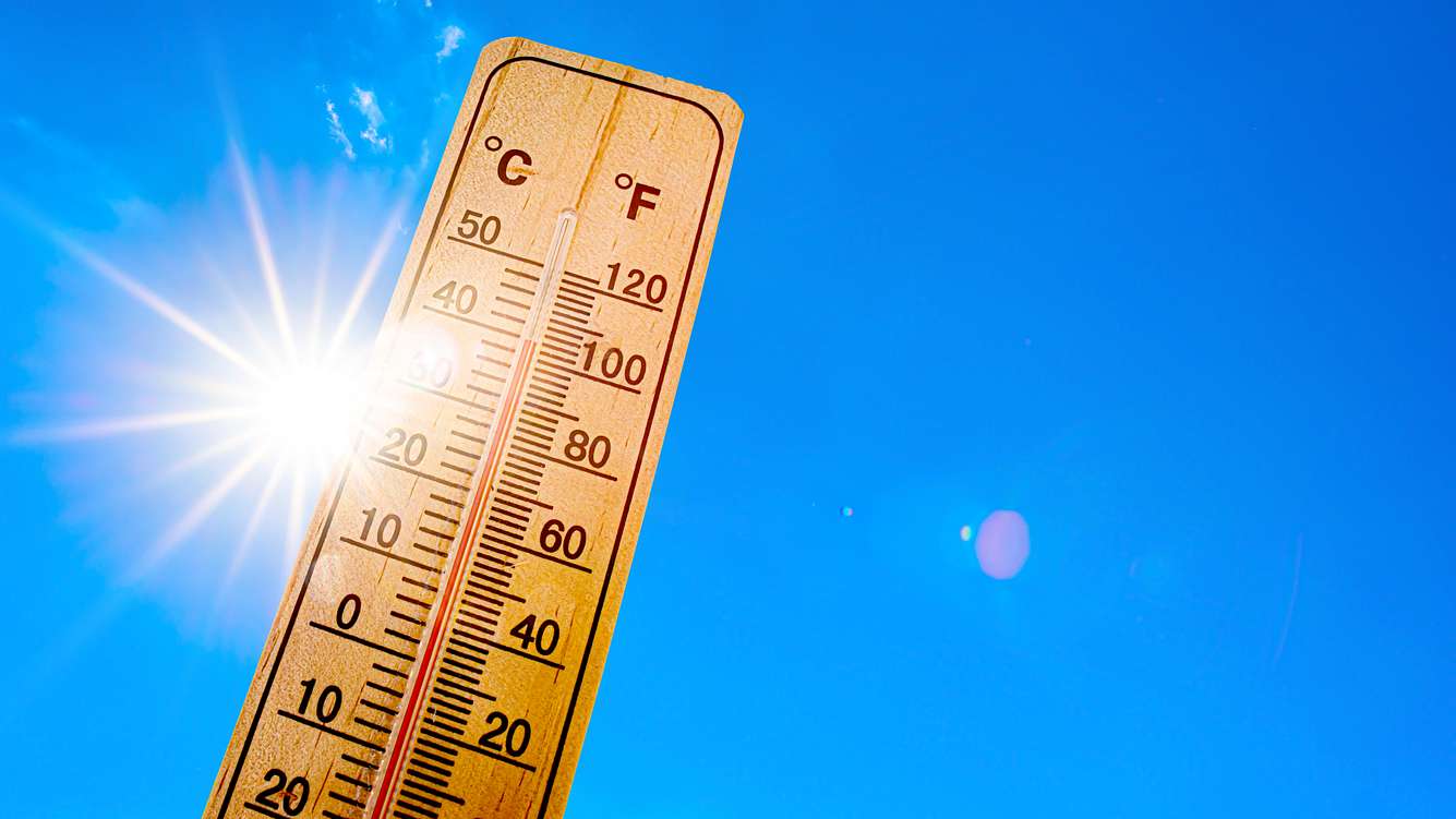 Meteorologen sagen einen ungewöhnlich heißen Juni-Monat voraus. Ein Holzthermometer vor blauem Himmel mit Sonnenschein.