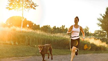 Eine Frau die mit ihrem Hund an der Joggingleine joggt - Foto: istock/eis:LSOphoto