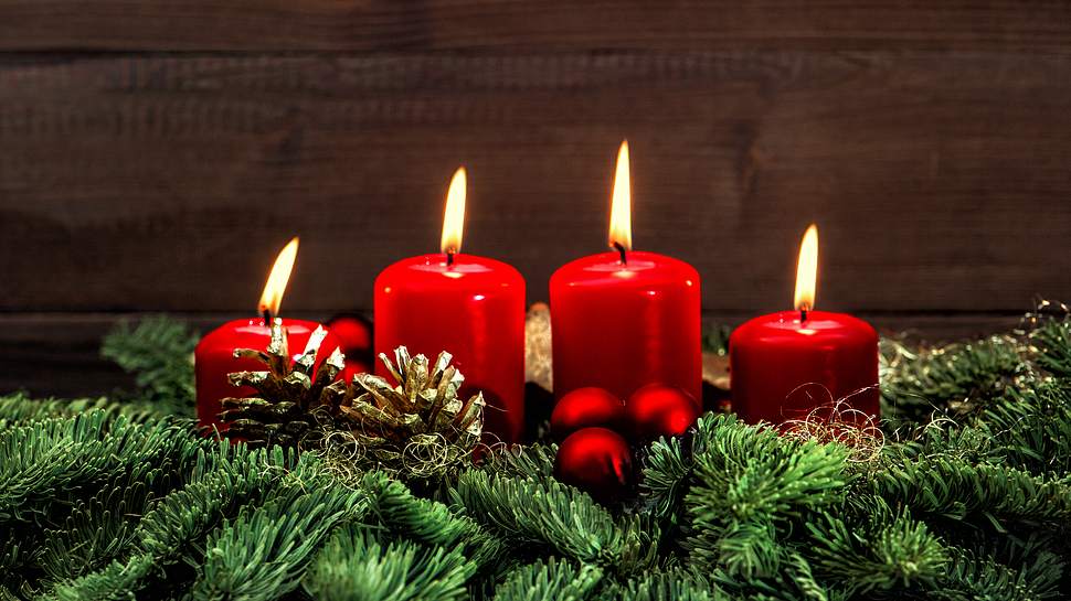 Ein klassisches Gesteck mit grünen Zweigen, roten Kugeln, goldenen Tannenzapfen und vier brennenden Kerzen - Foto: iStock/LiliGraphie