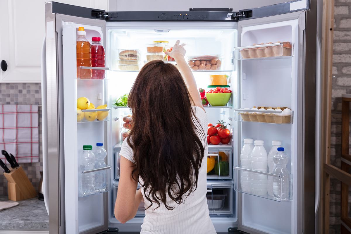 Frau steht vor dem Kühlschrank und greift nach einem Kühlschrank-Organizer