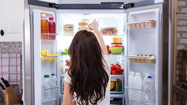 Frau steht vor dem Kühlschrank und greift nach einem Kühlschrank-Organizer - Foto: iStock/AndreyPopov