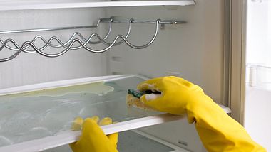 Frau reinigt das Innere eines Kühlschranks mit einem Schwamm. - Foto: Jevtic / iStock