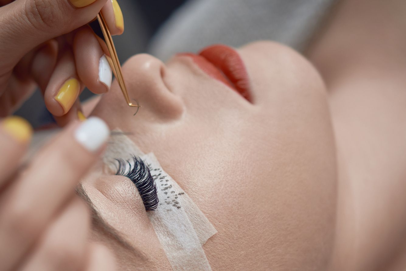 Künstliche Wimpern Kosmetikerin klebt künstliche Wimpern bei anderer Frau mit geschlossenen Augen an.