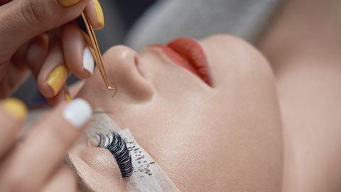 Kosmetikerin klebt künstliche Wimpern bei anderer Frau mit geschlossenen Augen an. - Foto: iStocke/stock_colors