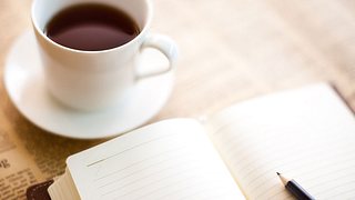 Tasse Kaffe und aufgeschlagenes Tagebuch.