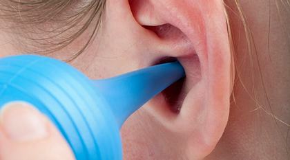 Frau reinigt ihr Ohr mit einer Ohrspritze.  - Foto: leschnyhan / iStock