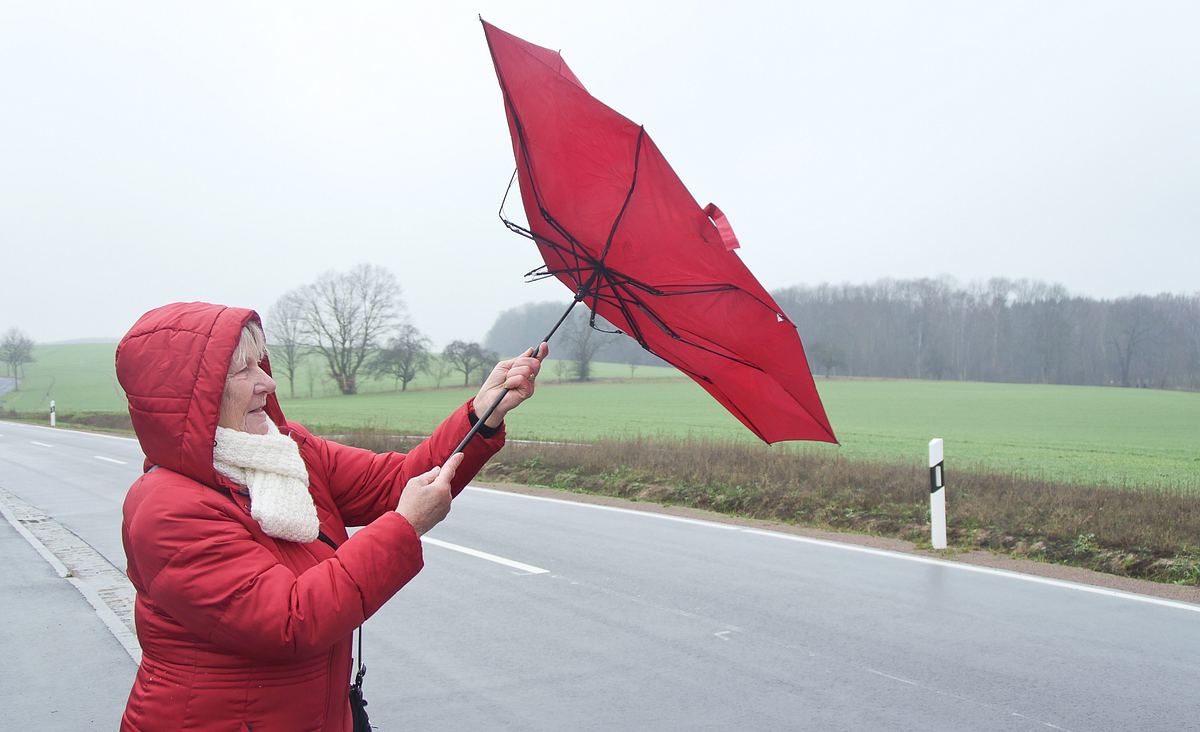 Eine Frau kämpft bei Wind und Niederschlag mit ihrem Regenschirm.
