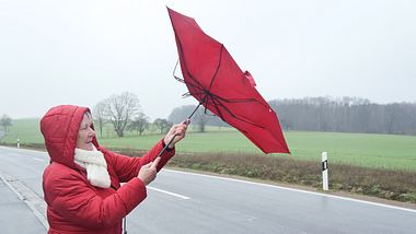 Eine Frau kämpft bei Wind und Niederschlag mit ihrem Regenschirm. - Foto: iStock / diephosi