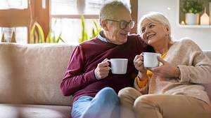 Ein älteres Ehepaar hat es sich mit Kaffeetassen auf der Couch gemütlich gemacht. - Foto: iStock / Piksel