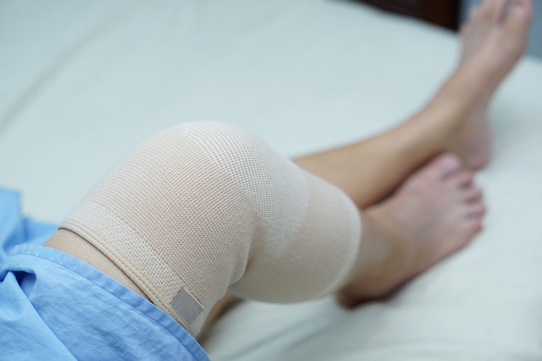 Frau liegt mit einem bandagierten Knie auf einem Bett.