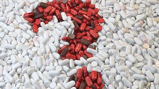 Weiße Tabletten in die ein Fragezeichen aus roten Tabletten gelegt ist. 