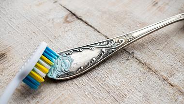 Silberbesteck wird mit Zahnbürste gereinigt. - Foto: Iryna Imago / iStock