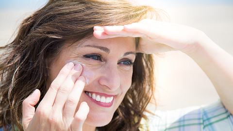 Frau cremt sich mit Sonnencreme für das Gesicht ein. - Foto: iStock/ ASIFE