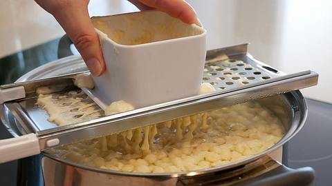 Spätzleteig wird mit einer Spätzlereibe in kochendes Wasser gerieben.  - Foto: nodramallama / iStock