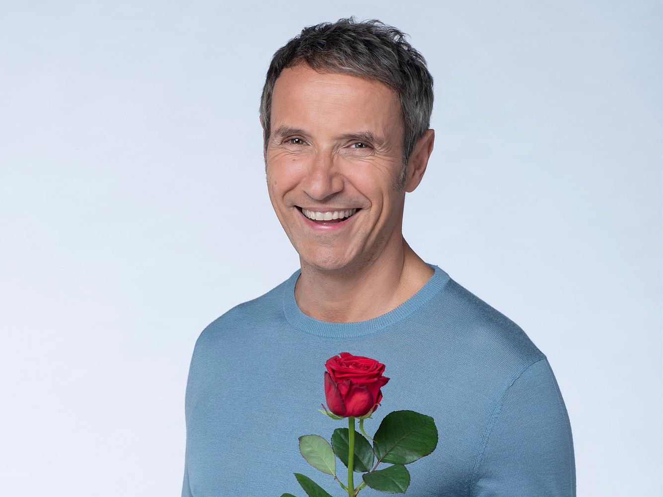 'Rote Rosen'-Star Stefan Plepp mit roter Rose in der Hand vor hellem Hintergrund