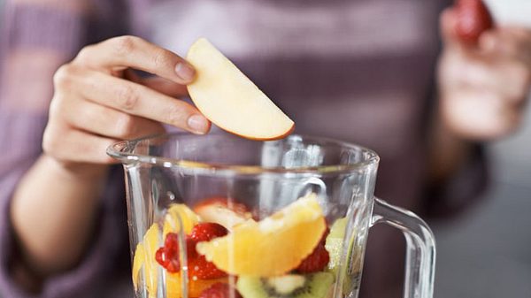 Eine Frau gibt frisches Obst in einen Standmixer.