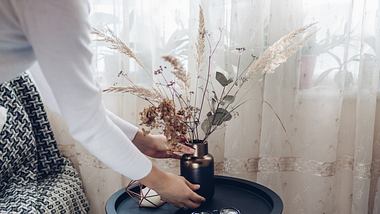 Frau stellt Trockenblumen Deko auf einen Tisch. - Foto: iStock/ Maryviolet