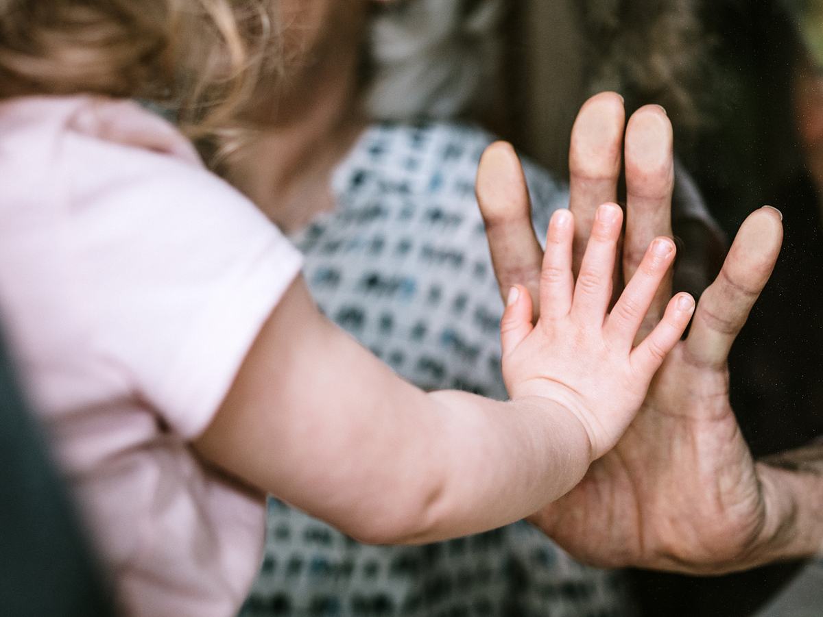 Kleines Mädchen drückt ihre Hand gegen eine Scheibe an Omas Hand.