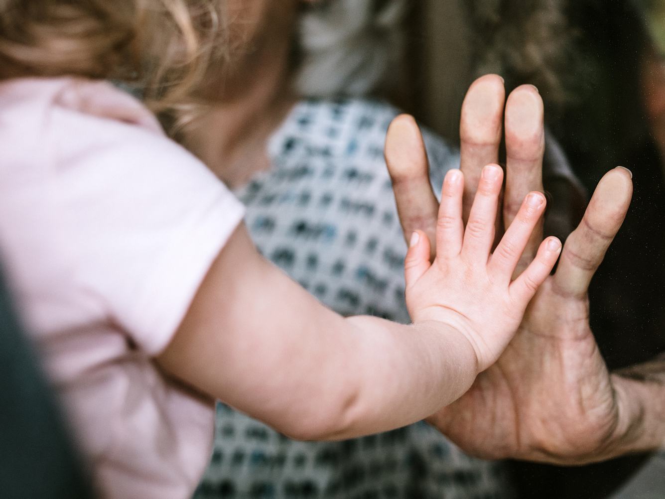 Kleines Mädchen drückt ihre Hand gegen eine Scheibe an Omas Hand. Kleines Mädchen drückt ihre Hand gegen eine Scheibe an Omas Hand.
