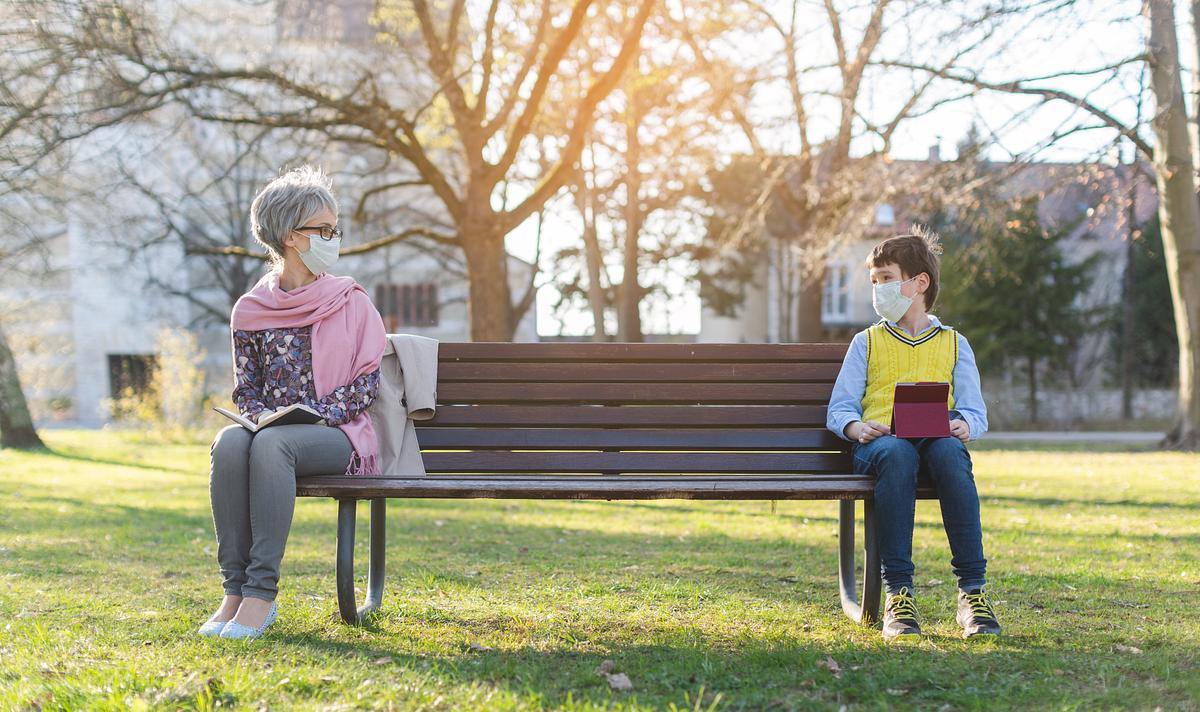 Eine Frau und ein Junge sitzen mit Abstand auf einer Parkbank.