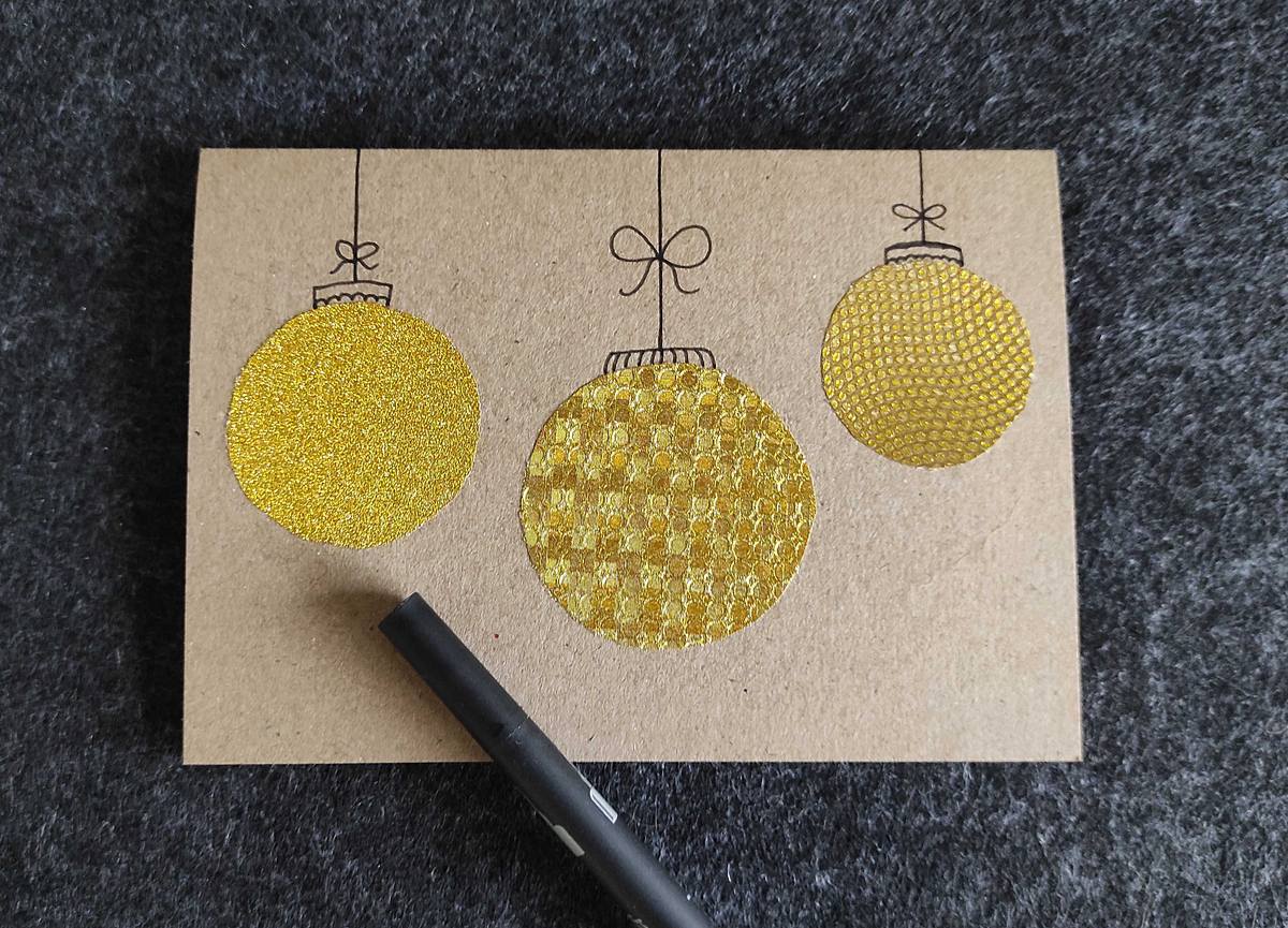 Weihnachtskarte mit drei goldenen Kugeln und einem Filzstift.